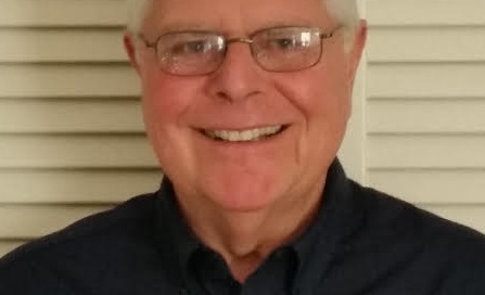 An older man smiling in front of a window.