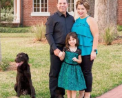 A family posing in front of a brick house with a dog.