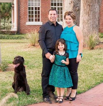 A family posing in front of a brick house with a dog.