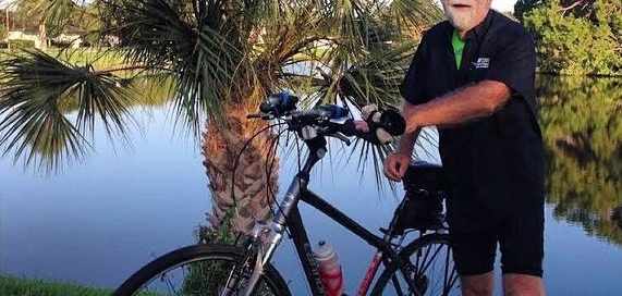 A man standing next to a bike next to a pond.